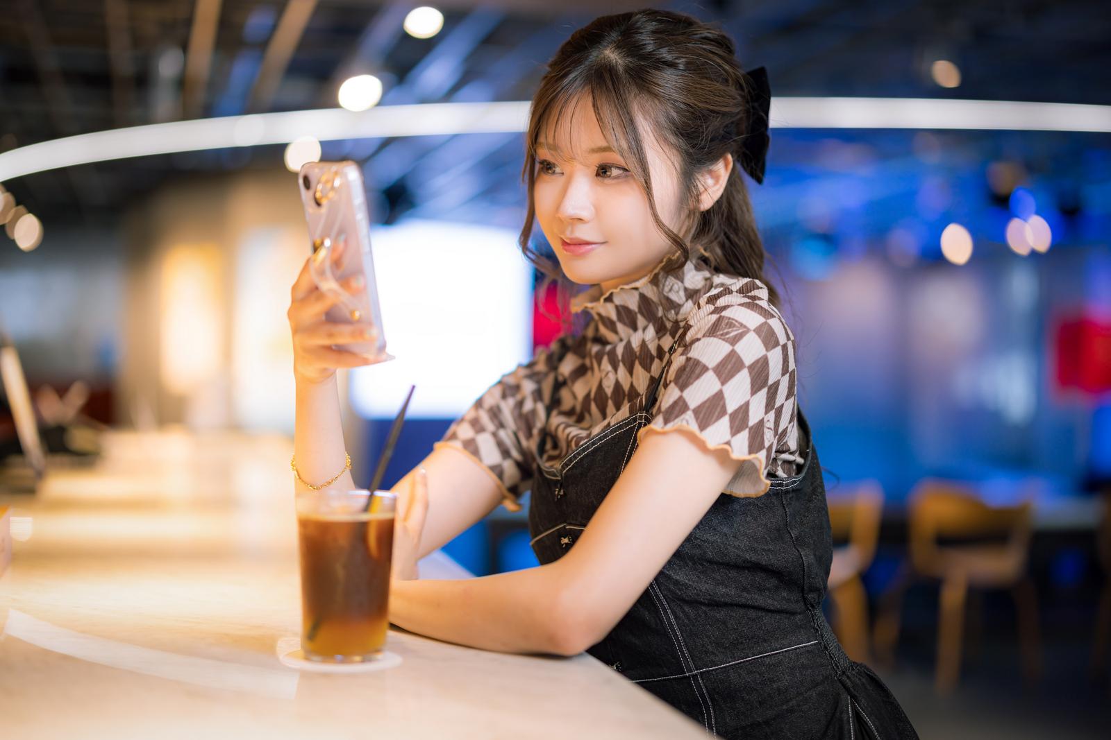 カフェのカウンター席でドリンクを持ちながらスマホを見る女性［モデル：れいか氏］