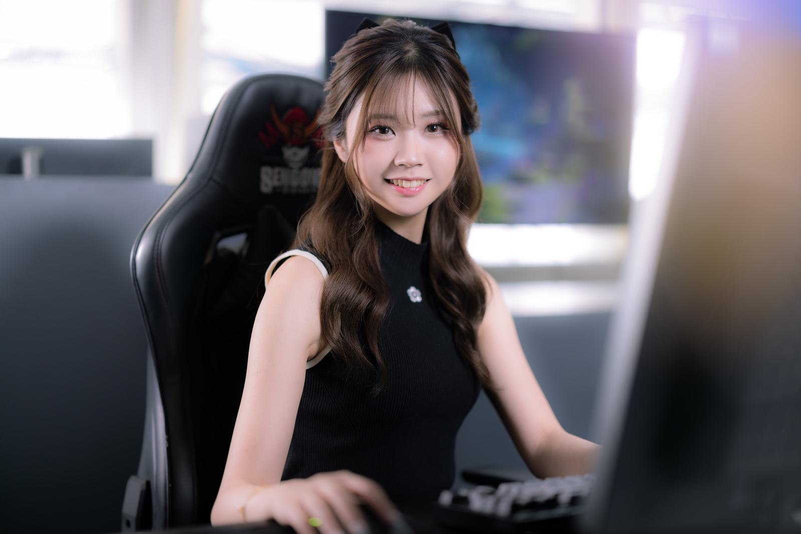 黒いゲーミングチェアに座り、パソコンのモニター前でカメラを見る笑顔の女性YouTuber［モデル：れいか氏］