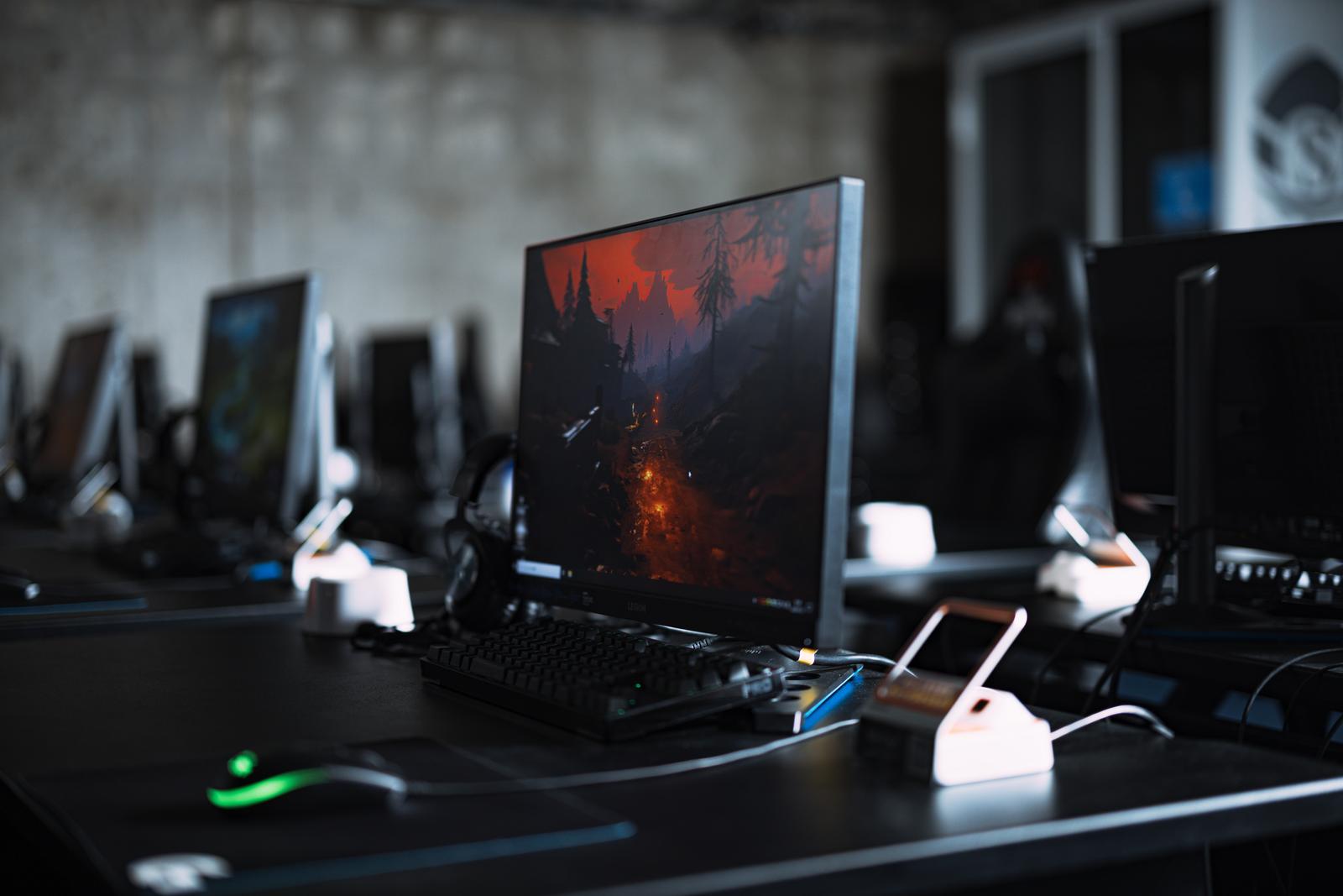 黒いデスクに並んだゲーミングPCとモニターが複数台配置されたeスポーツ施設