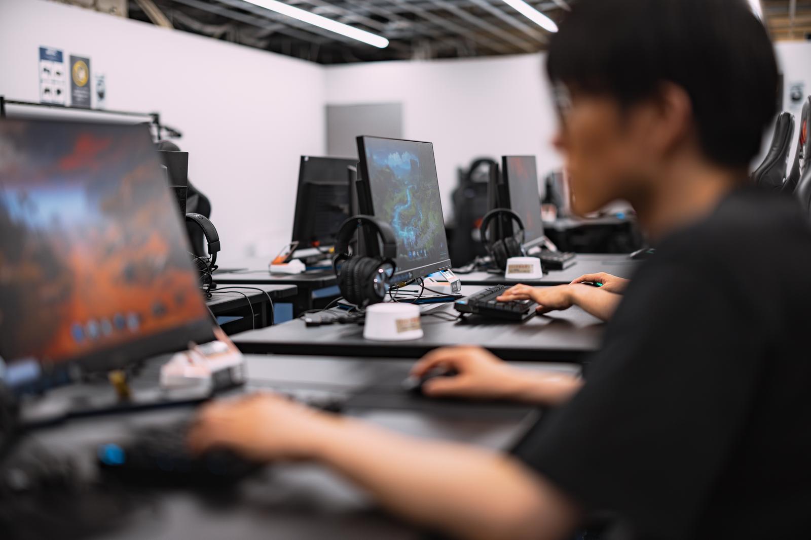 ゲーミングPCと複数のディスプレイが並ぶeスポーツ会場でプレイヤーがキーボードを操作している
