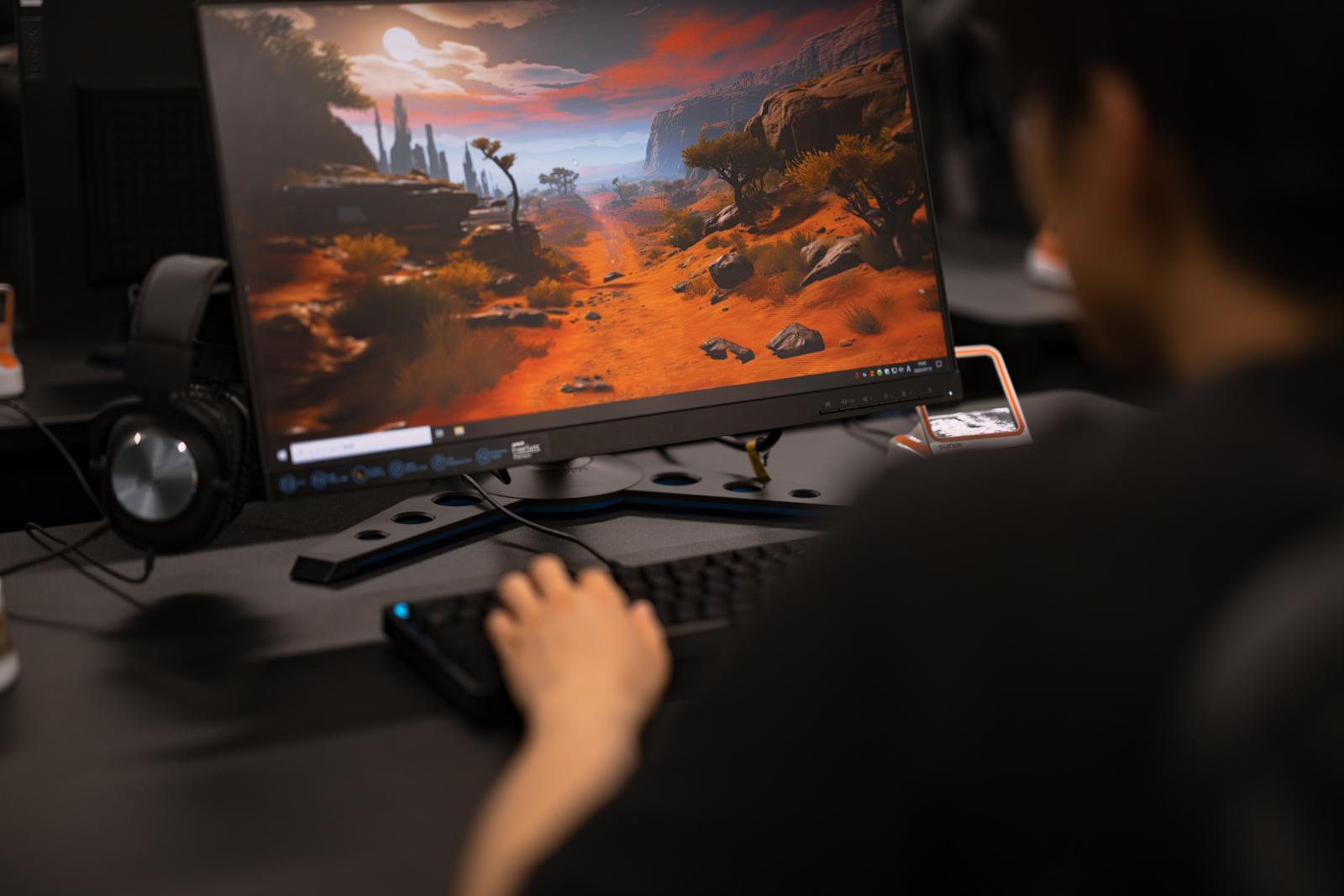 モニターに砂漠のゲーム画面を表示させながらFPSをプレイするゲーマーの手元