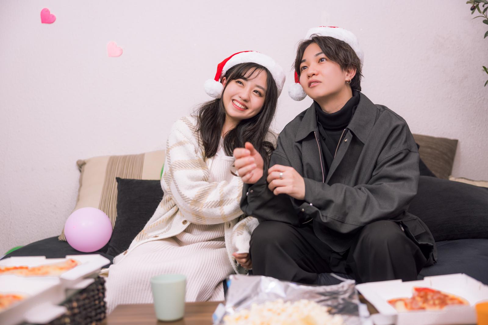 サンタ帽をかぶったカップルがクリスマスパーティをリビングで楽しんでいる［モデル：河村友歌 SHUN］