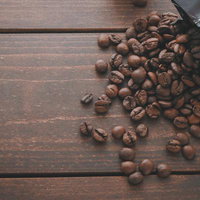 黒いパッケージから溢れる焙煎したコーヒー豆が散らばる木製テーブルの写真