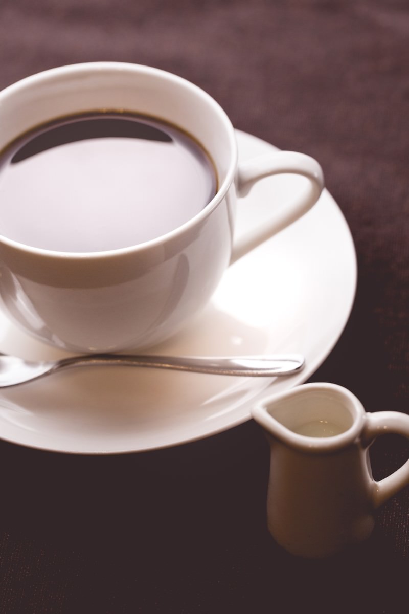 白いカップのコーヒーとミルクピッチャー、スプーンのテーブルウェア