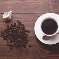 木製テーブルに散らばるコーヒー豆と淹れたてのコーヒーの写真