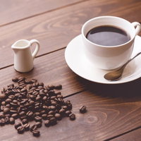 散らばるコーヒー豆と淹れたてのコーヒーが入ったカップの写真