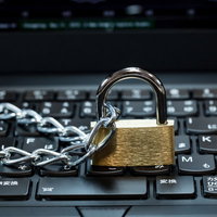 ノートパソコンのキーボードの上に置かれた南京錠と鎖の写真