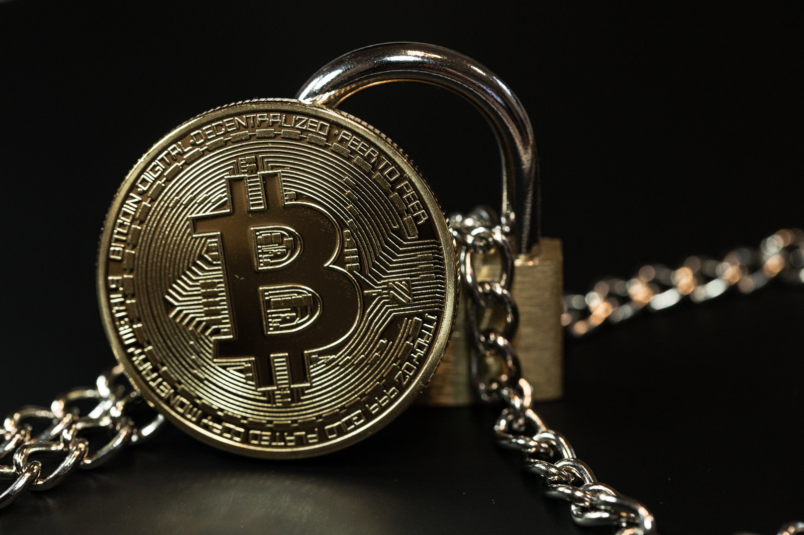金属の鎖に繋がれた金色のビットコインコインと南京錠