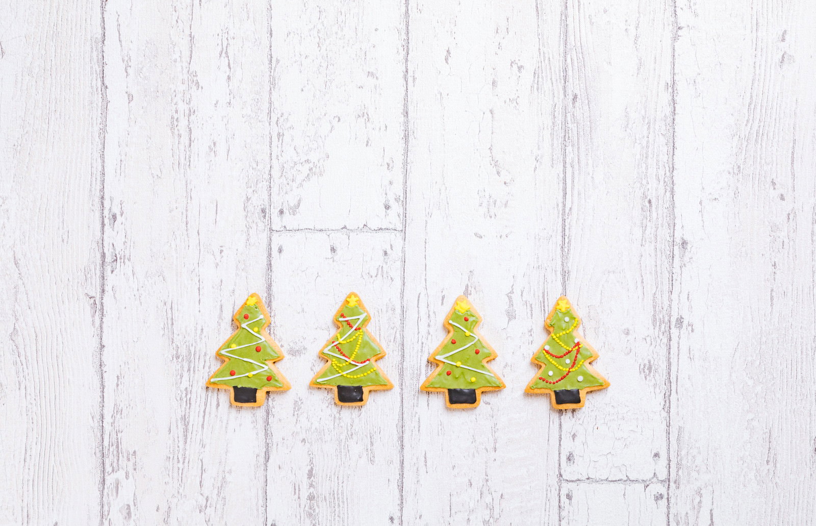 白い木目調の背景に並んだ緑色のクリスマスツリー型アイシングクッキー