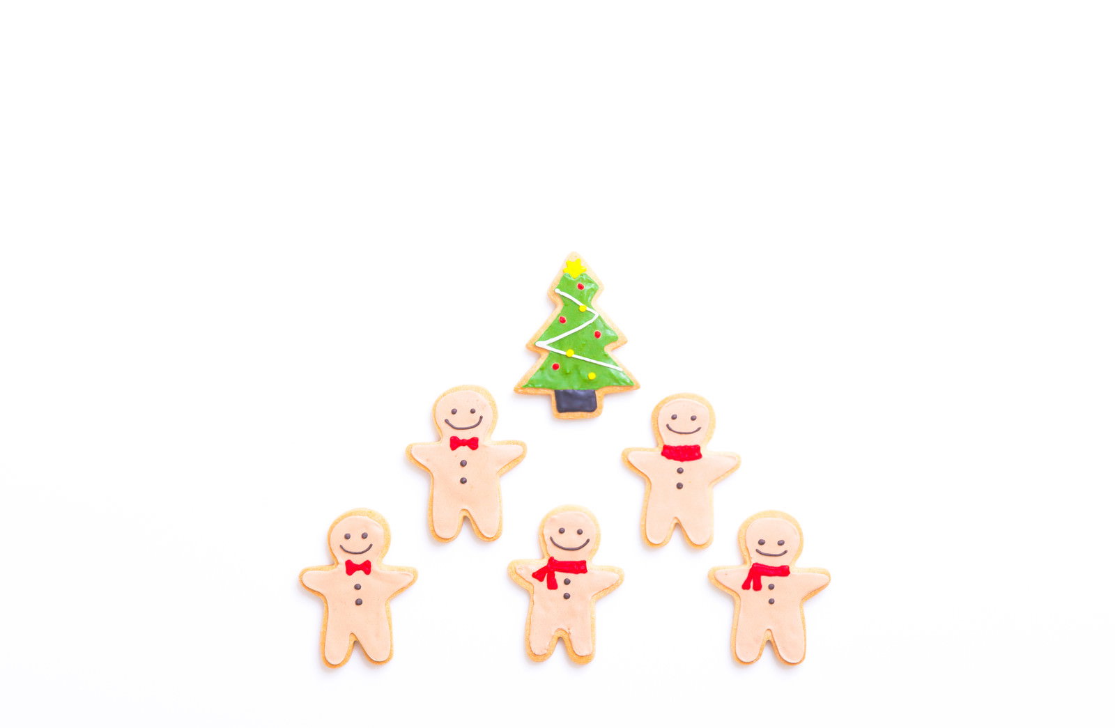白い背景に緑のクリスマスツリーと笑顔の人型アイシングクッキーが並んでいる