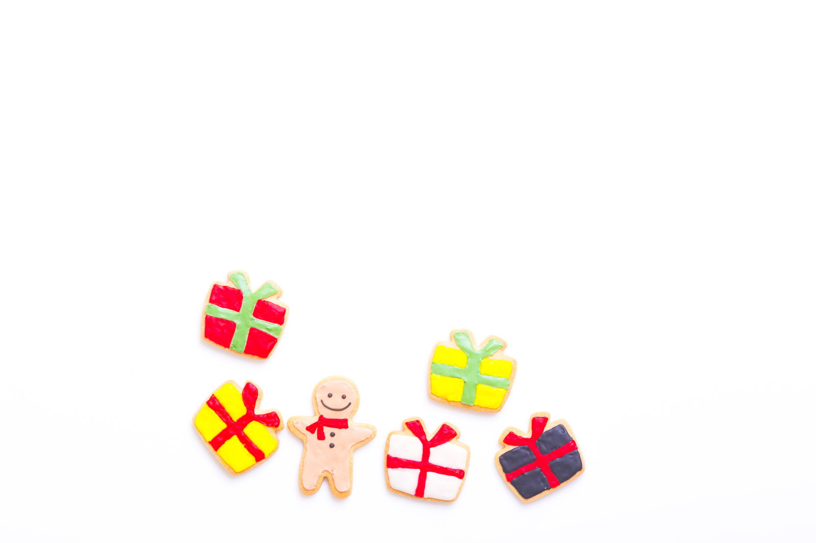 白い背景にクリスマスプレゼントのギフトボックスとカラフルなアイシングクッキーが並んでいる