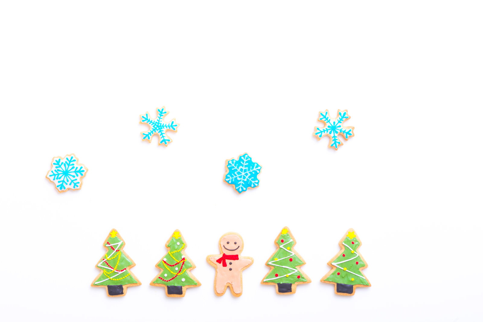 白い背景に配置されたピンクのアイシングクッキーと緑のクリスマスツリー、青い雪の結晶
