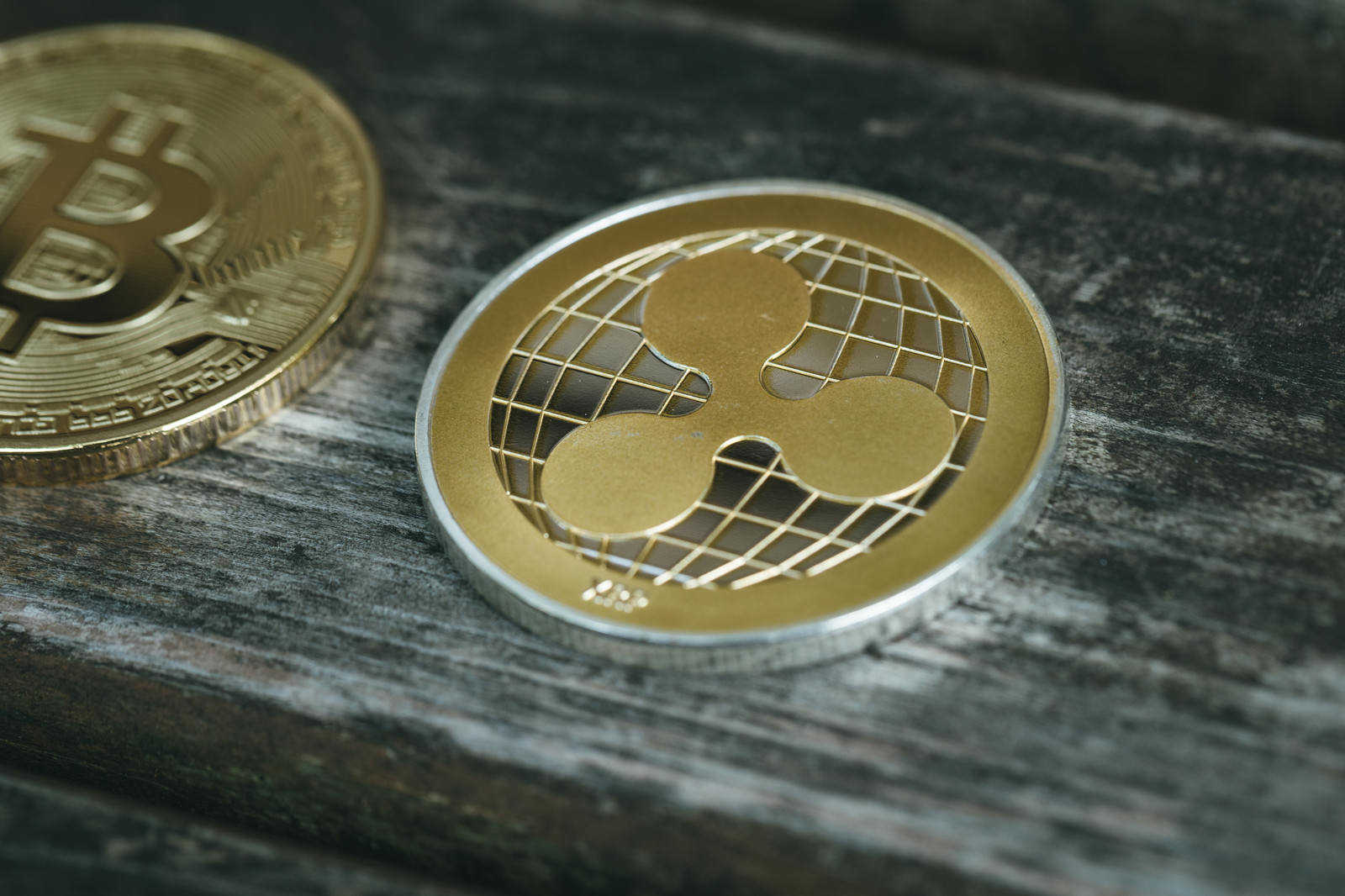 木製テーブルの上に置かれたビットコインとリップルの金色のコイン