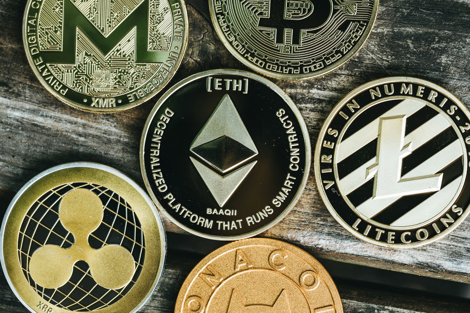 木製テーブルの上に並べられたイーサリアム、ビットコイン、ライトコインなどの暗号通貨コイン