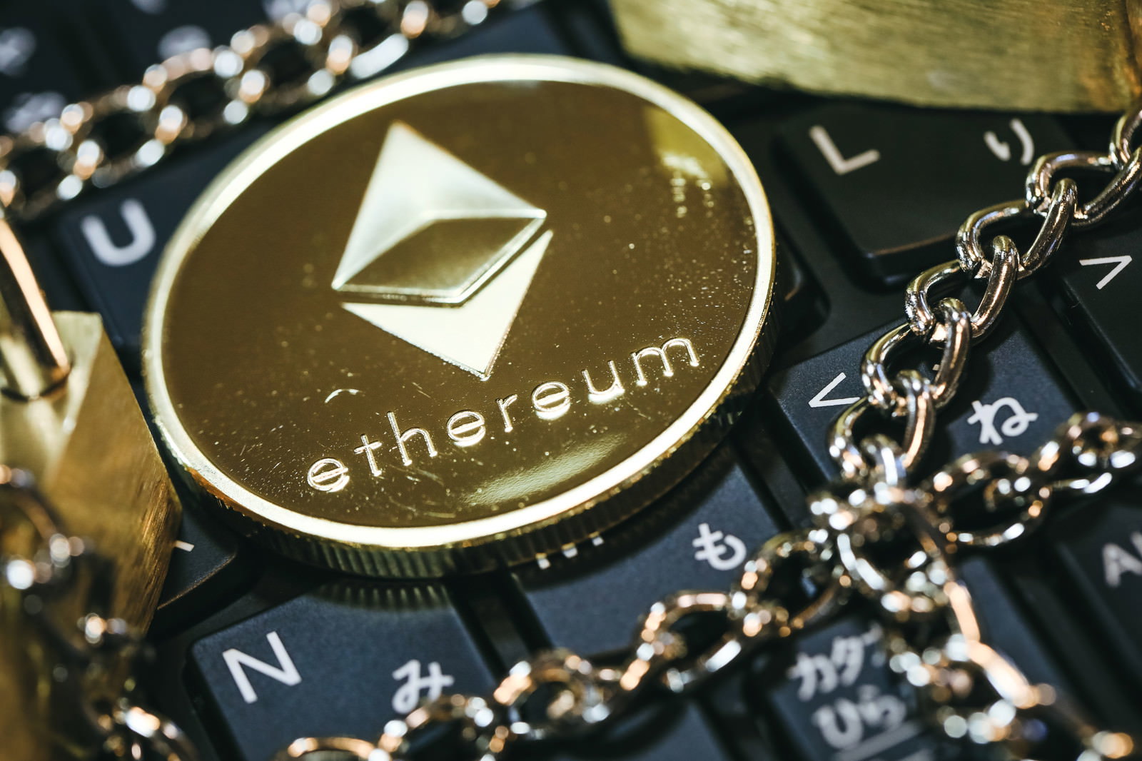 黒いキーボードの上に置かれた金色のチェーンとETHロゴ入りコイン