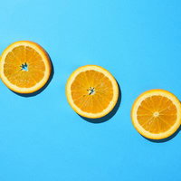 青色の背景に並ぶ輪切りオレンジの断面の写真