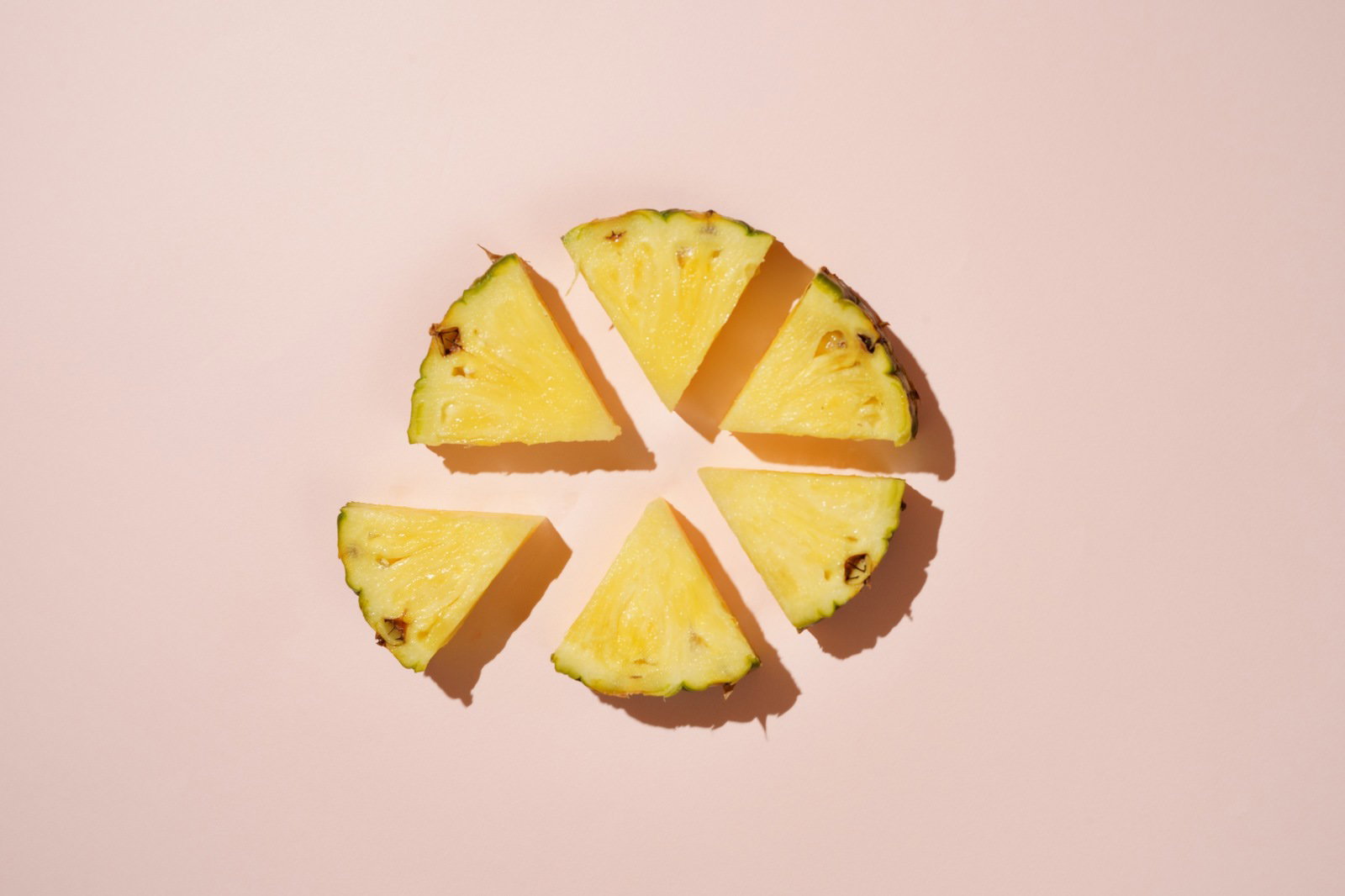 ピンク色の背景に6等分にカットされた黄色いパイナップルが円形に配置されている