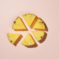 ピンク色の背景に円形に配置されたカットパイナップルの写真