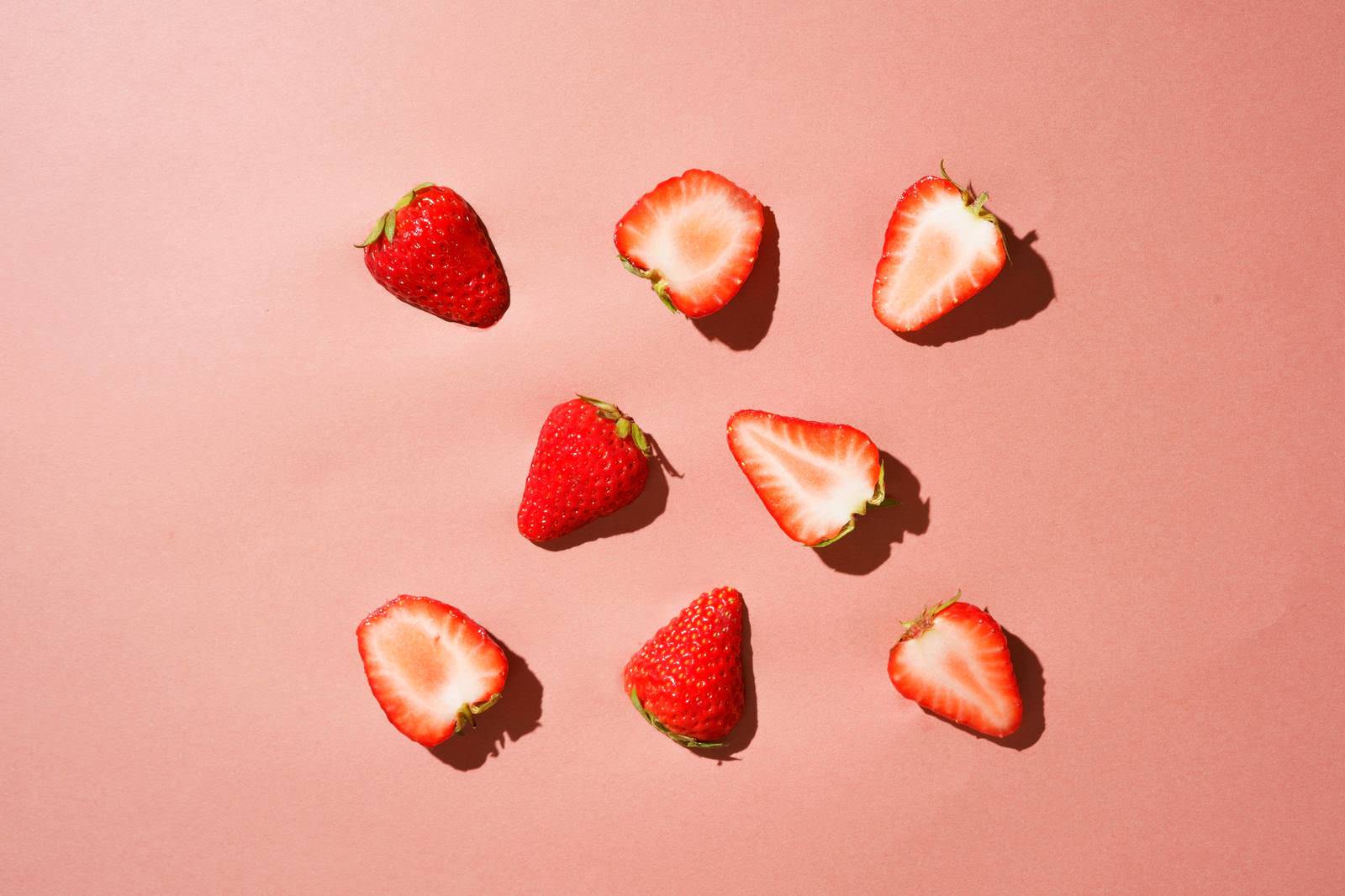 ピンクの背景にカットされたいちごが並んでいる様子