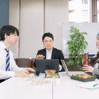 昼食を取りながら会議するビジネスマンと女性社員の写真