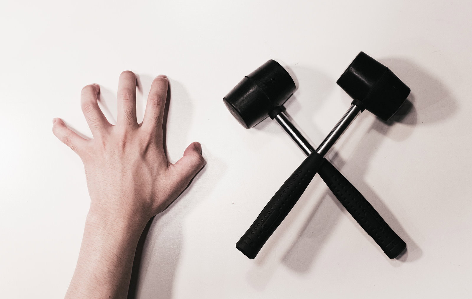 白い背景に人の手の爪痕と黒いハンマー2本がクロスして配置された写真