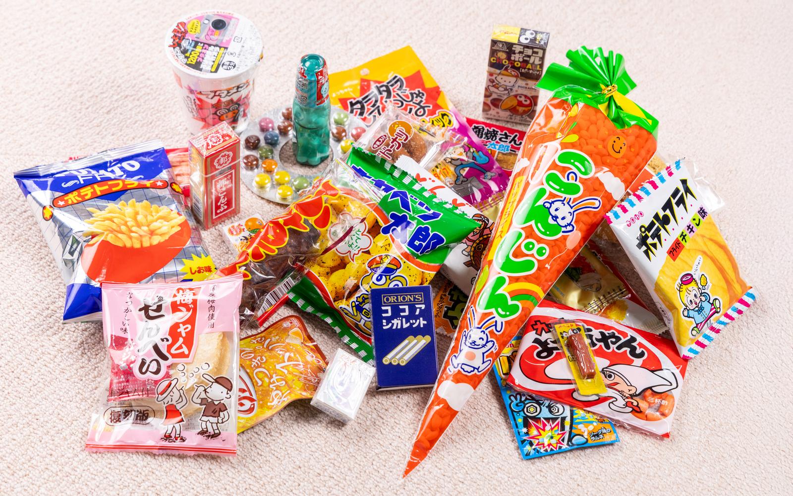 100円以下のスナック菓子と飲料がカラフルなパッケージで白い背景に並んでいる