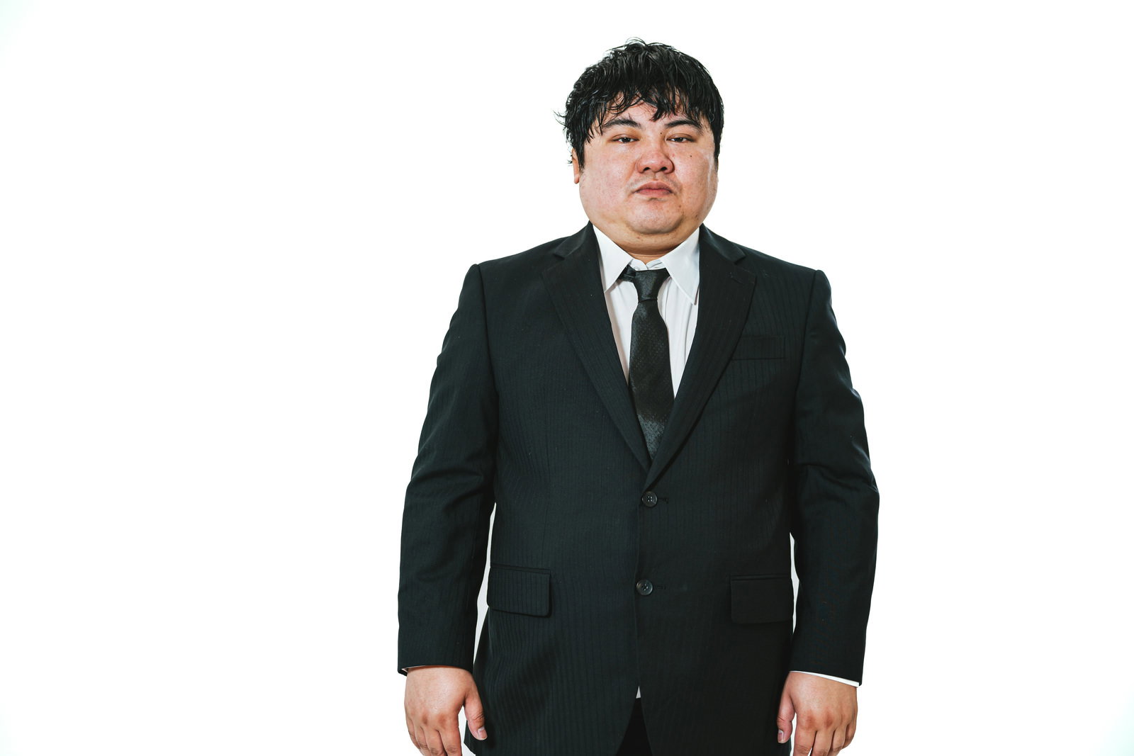濃いグリーンのスーツを着て不機嫌そうな表情をする会社員男性［モデル：段田隼人］