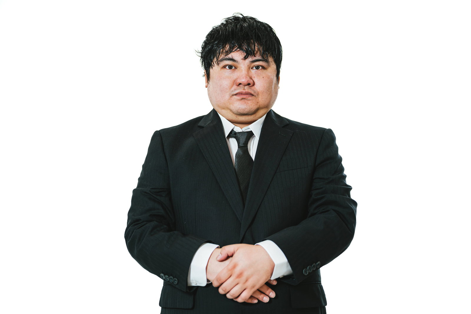黒いスーツを着て手を組み真摯な表情を見せる男性会社員［モデル：段田隼人］
