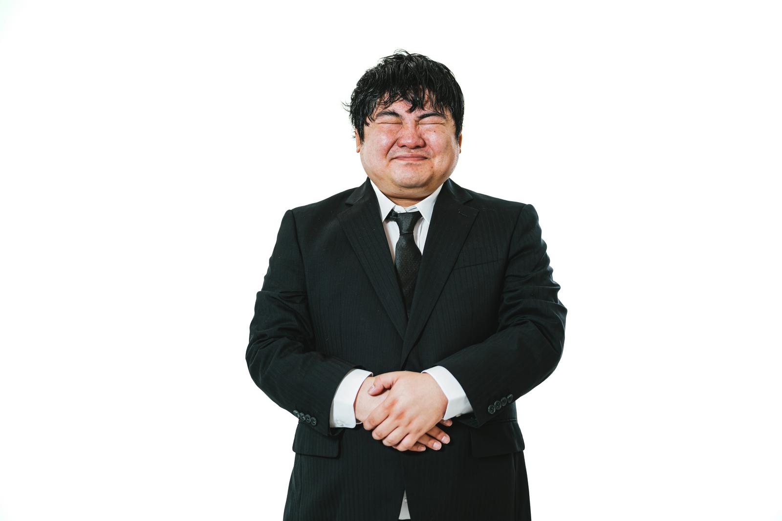 黒いスーツを着て手を組み、おもてなしのポーズをとる男性［モデル：段田隼人］
