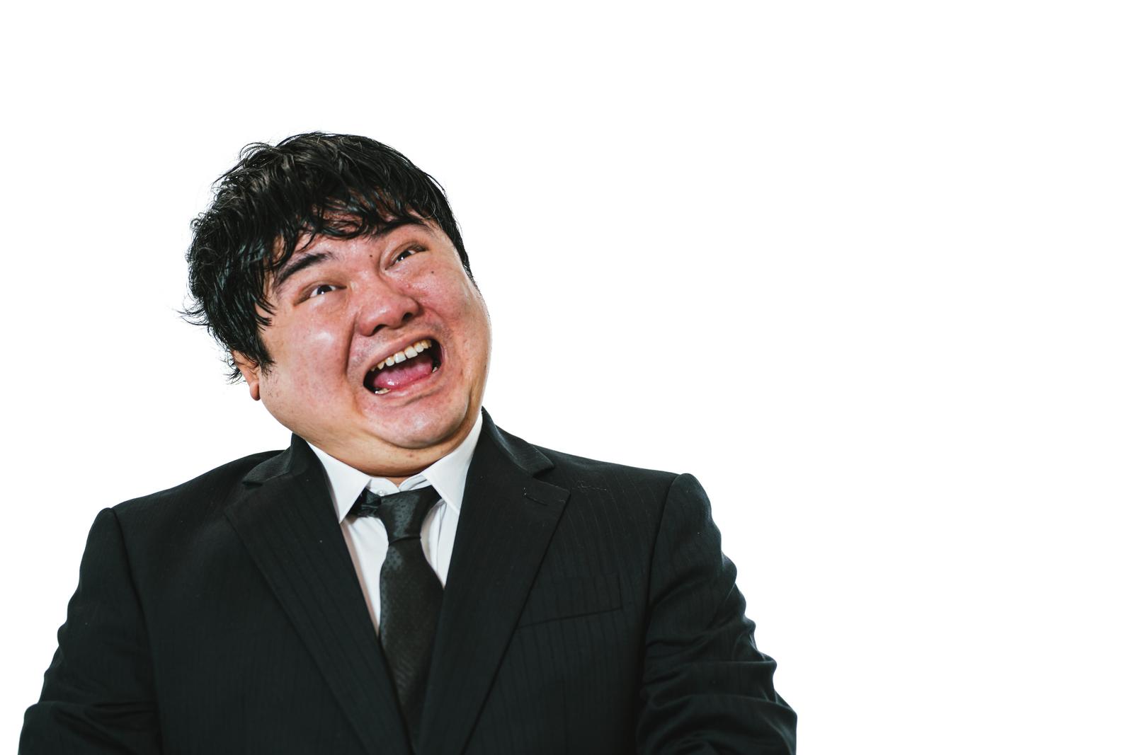 白背景で髪を乱しながら口を大きく開けて引きつり笑いするスーツ姿の男性［モデル：段田隼人］