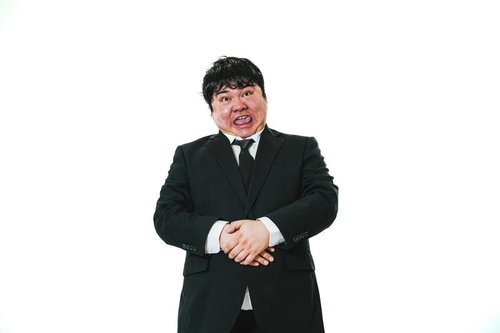 黒いスーツを着た男性が驚いた表情で腕組みをする