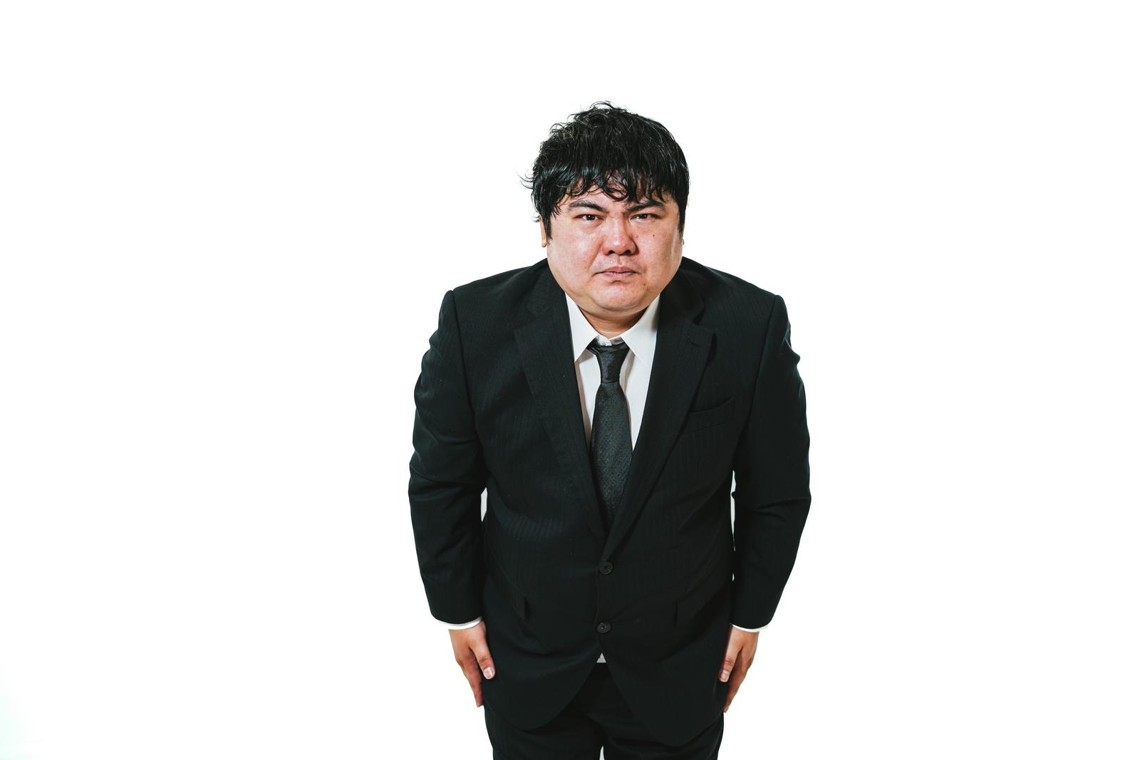 黒いスーツを着た男性が両手を下げて謝罪している［モデル：段田隼人］