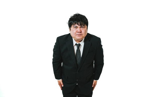 黒いスーツを着た紺色ネクタイの男性が謝罪するポーズをとる