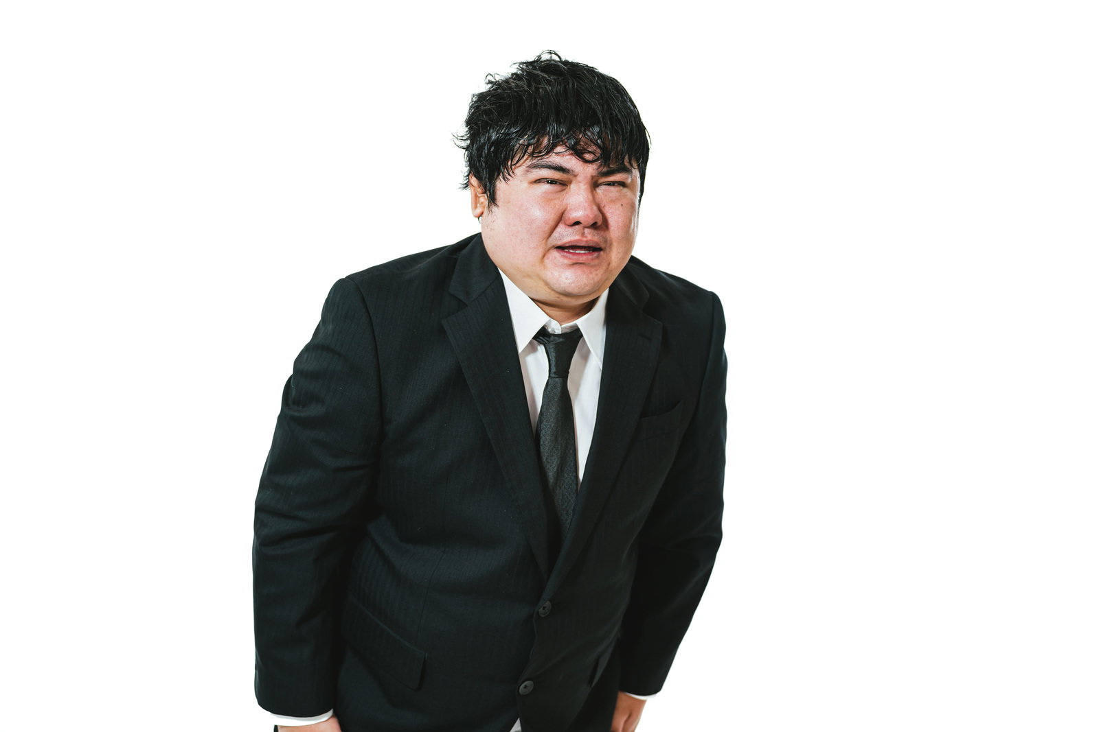 黒いスーツを着た男性が困惑した表情で頭を下げて謝罪している［モデル：段田隼人］
