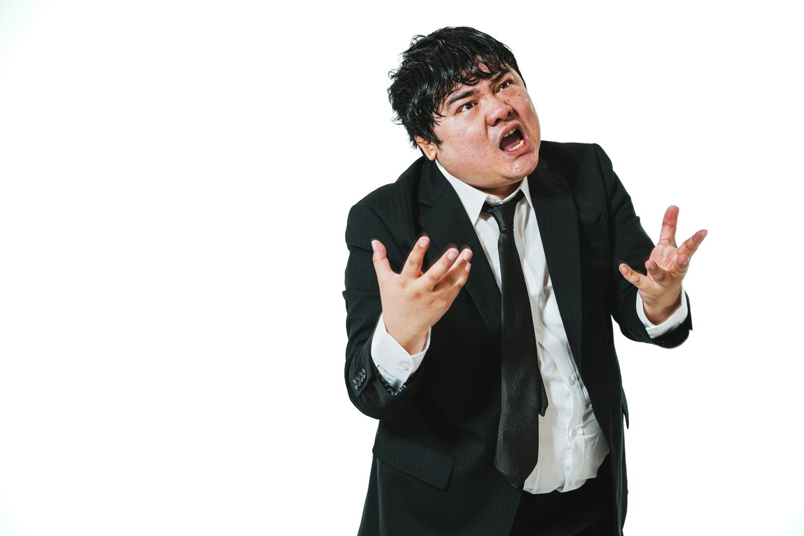 白背景の前で両手を広げて口を大きく開け激怒しているスーツ姿の男性会社員［モデル：段田隼人］