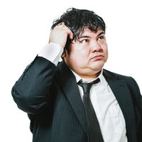 頭をかきながら悩むスーツ姿の会社員の写真