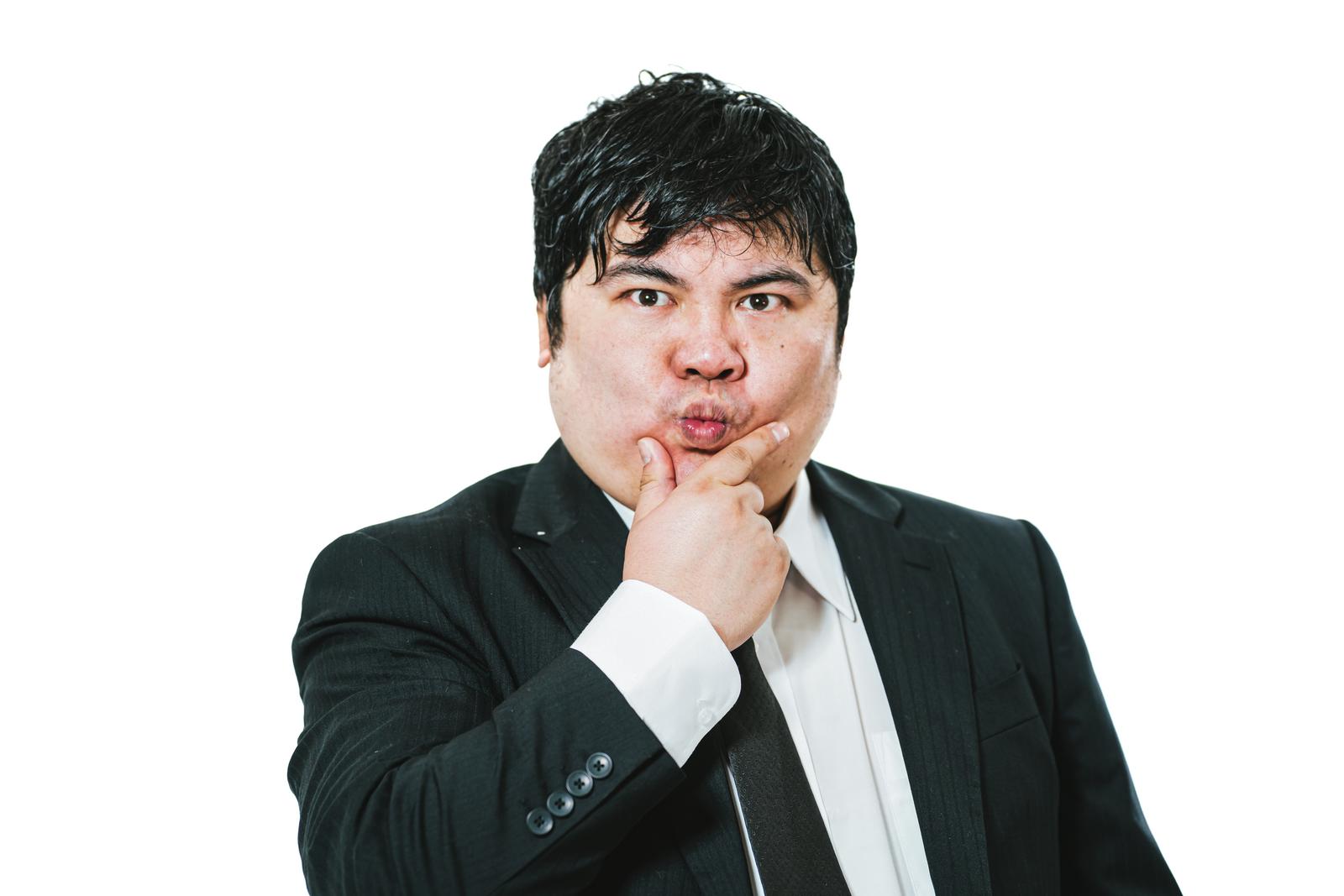 A businessman in a suit with his hand on his chin and mouth slightly pursed, thinking deeply in front of a white background