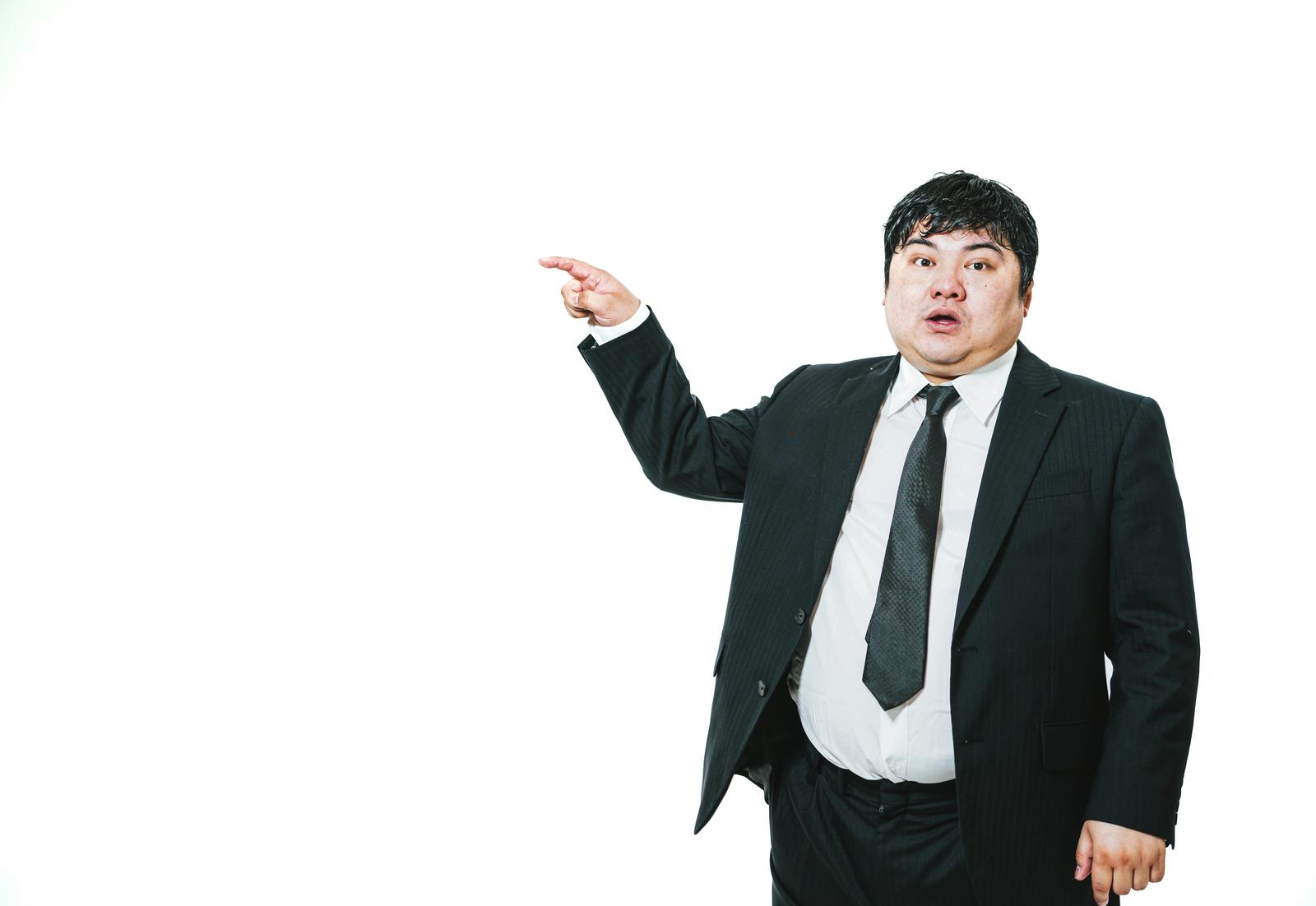 An overweight businessman in a suit with his mouth open, pointing to the left against a white background