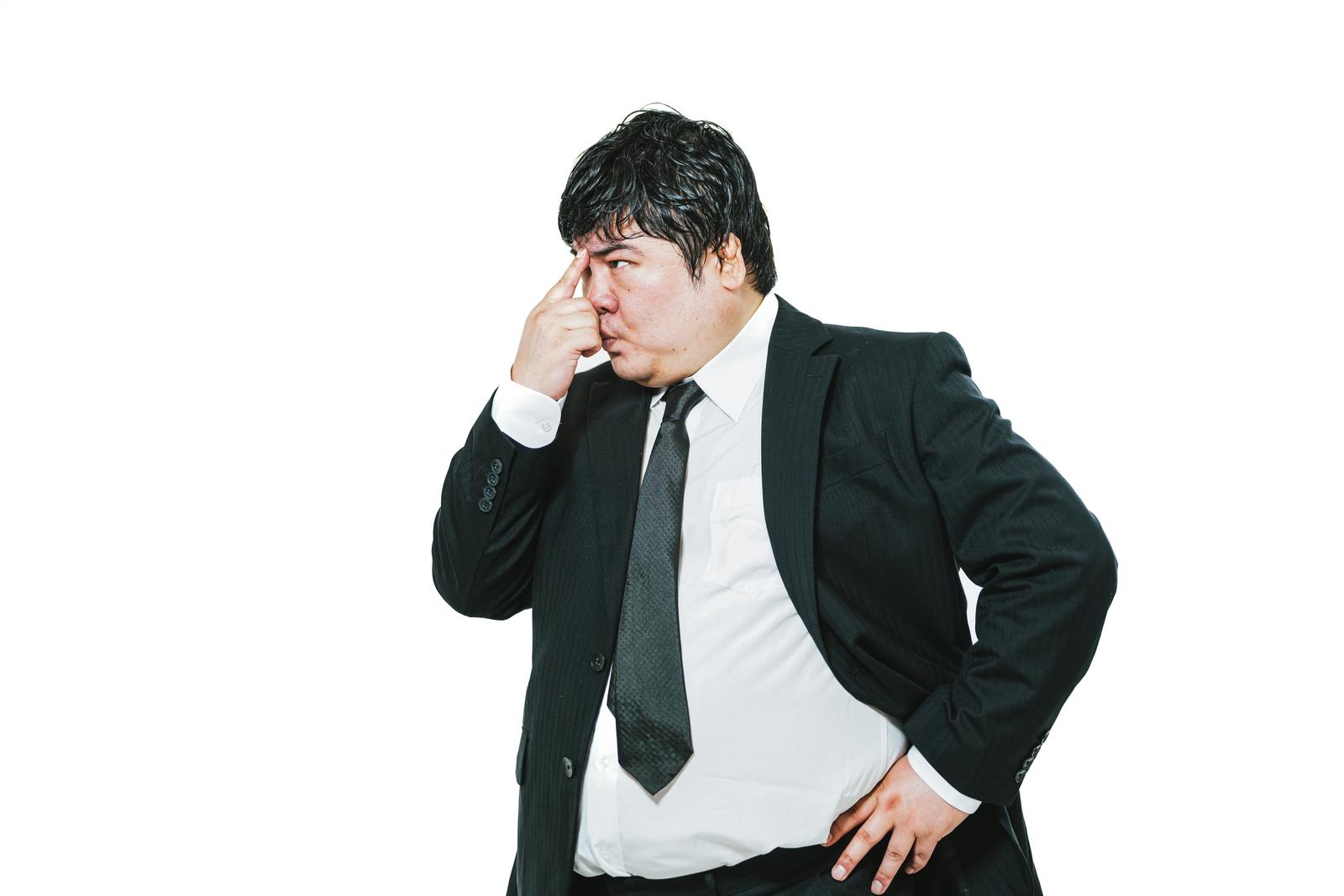 Businessman in suit turned to the side with finger beside his nose, contemplating in front of white background