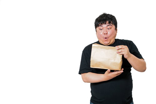 黒いTシャツ姿で茶色い紙袋を開封して驚く男性の表情