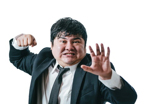 攻撃から身を守る防御ポーズをとるスーツ姿の弱々男子