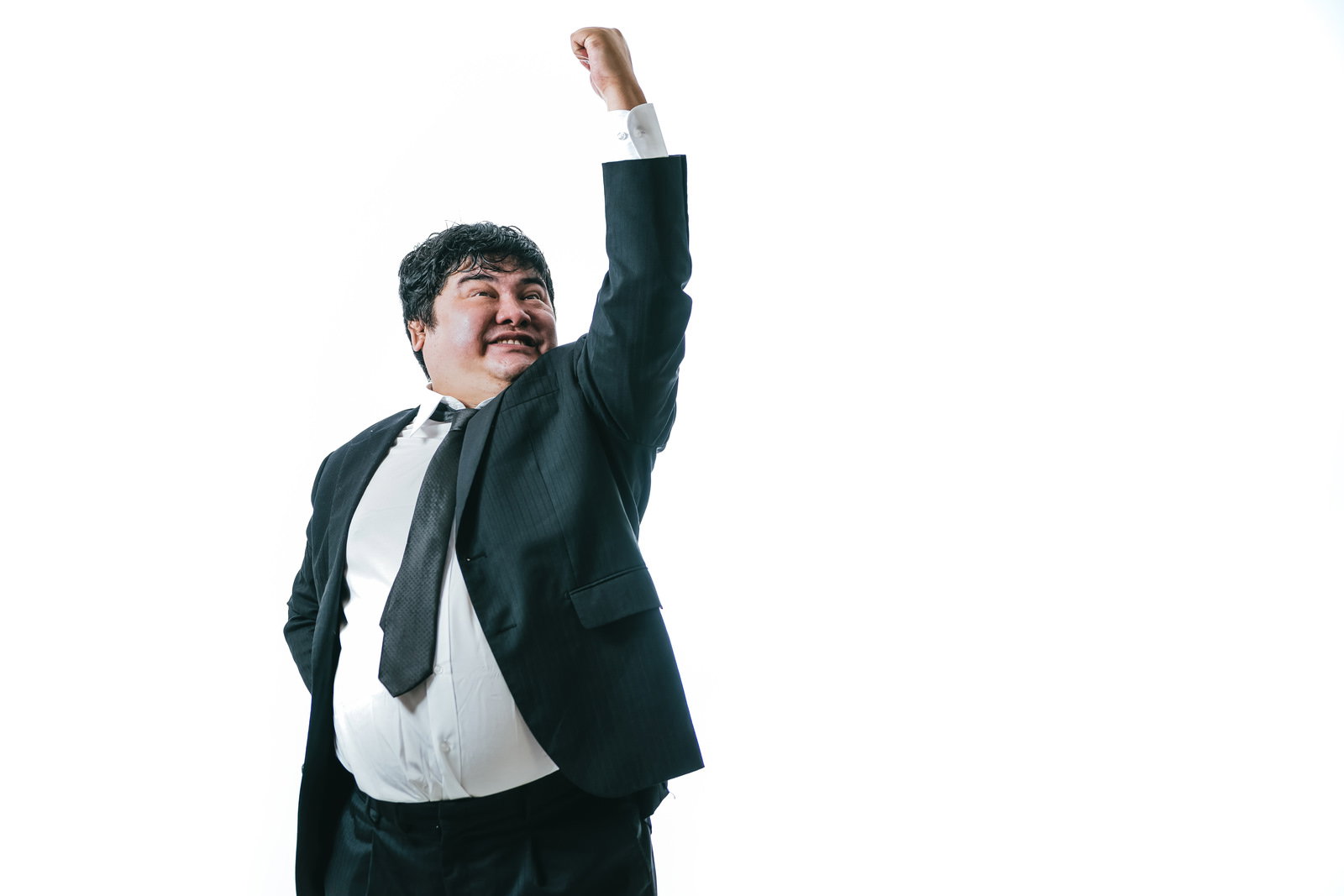 黒いスーツを着た男性が片手を天に向けて突き上げるガッツポーズをしている［モデル：段田隼人］