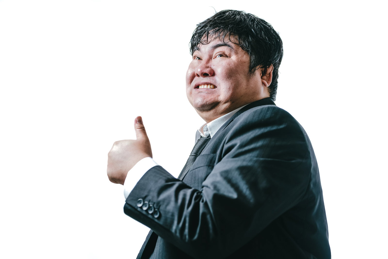 黒いスーツを着た男性が親指を立てるポーズをする様子［モデル：段田隼人］