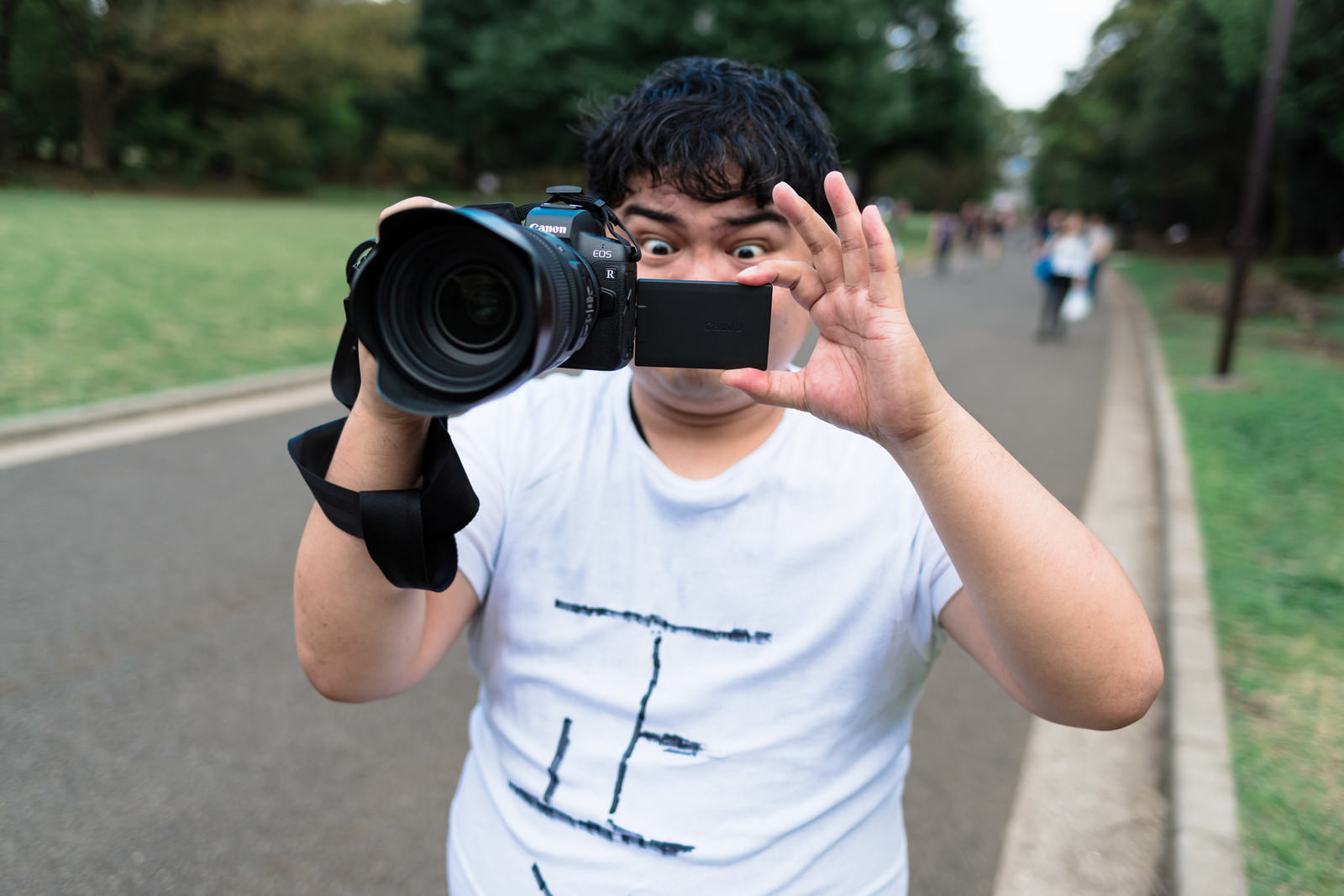 ミラーレス一眼カメラで撮影する白Tシャツの男性カメラマン［モデル：段田隼人］