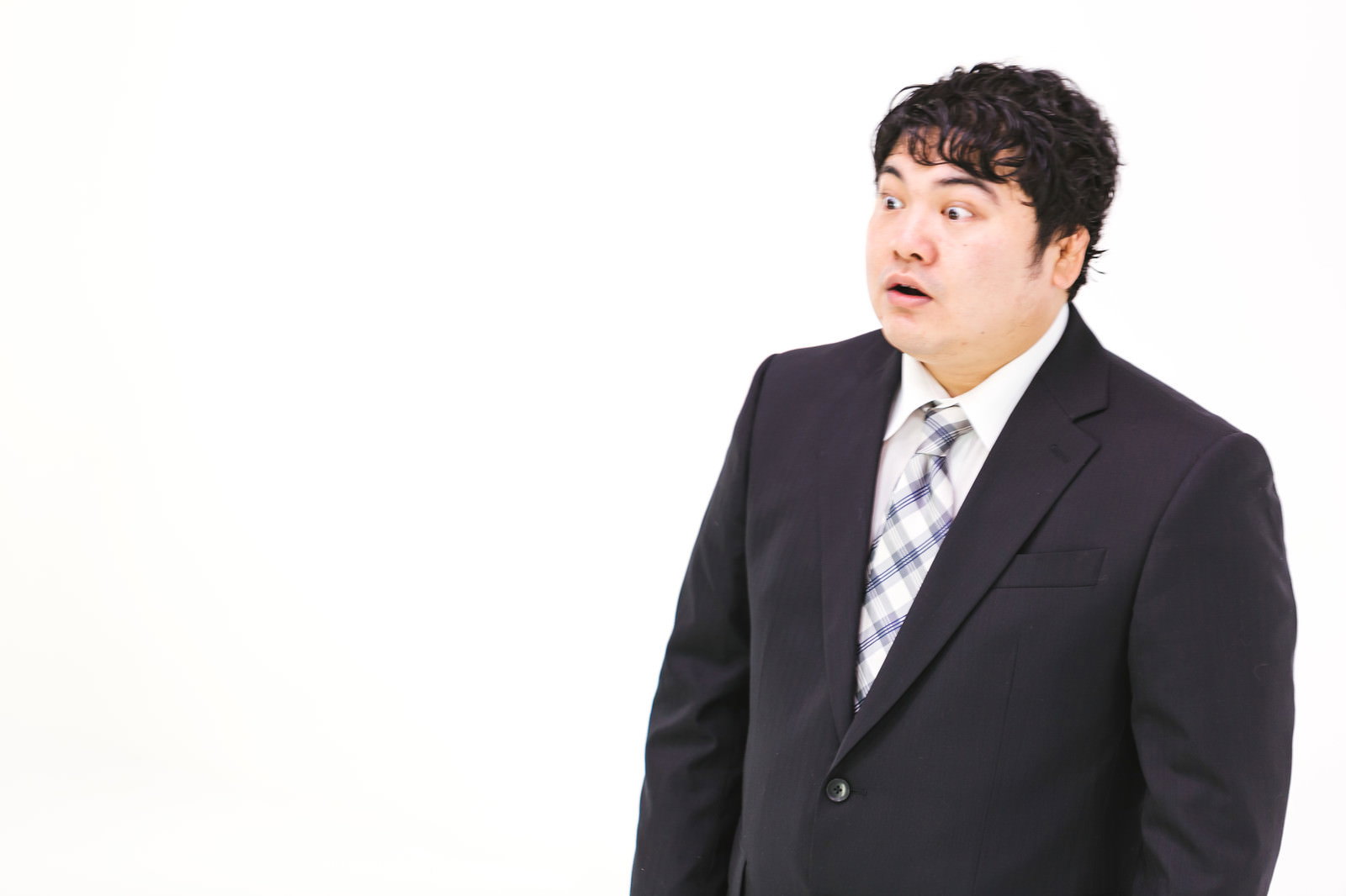 黒いスーツを着た男性が、驚きの表情で口を開けている［モデル：段田隼人］
