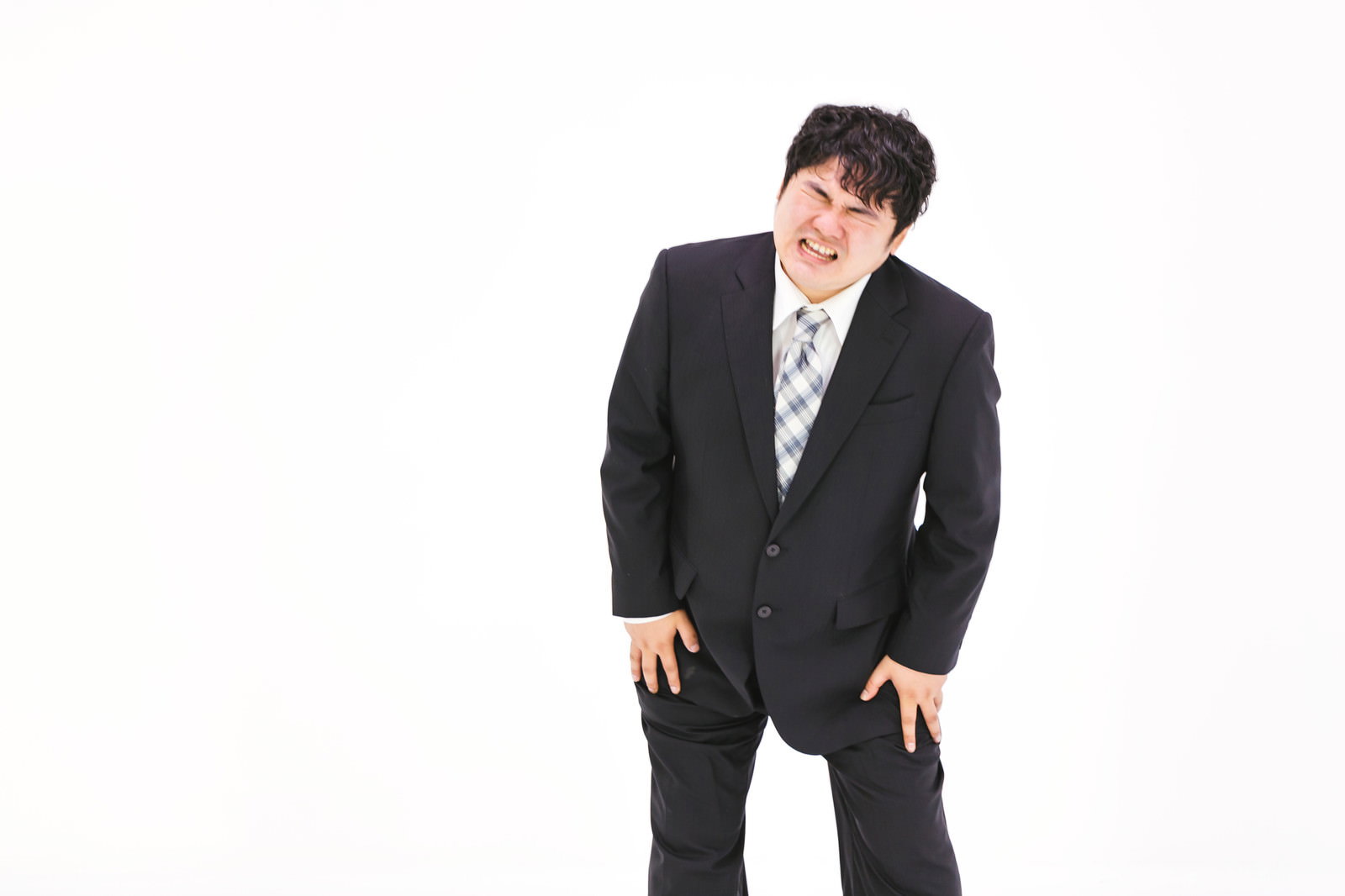 膝を痛めて苦痛な表情を浮かべる黒いスーツ姿の男性［モデル：段田隼人］