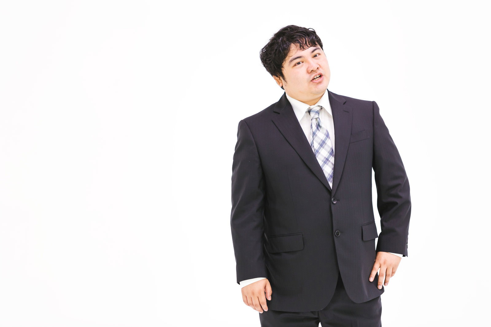スーツを着た男性が上を向いて思案しながら立っている［モデル：段田隼人］