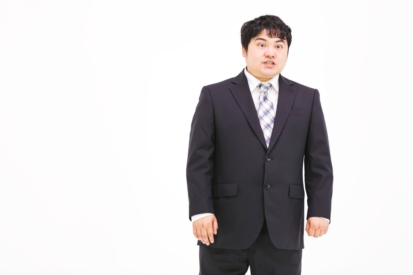 驚いた表情で両目を見開く黒いスーツの男性［モデル：段田隼人］