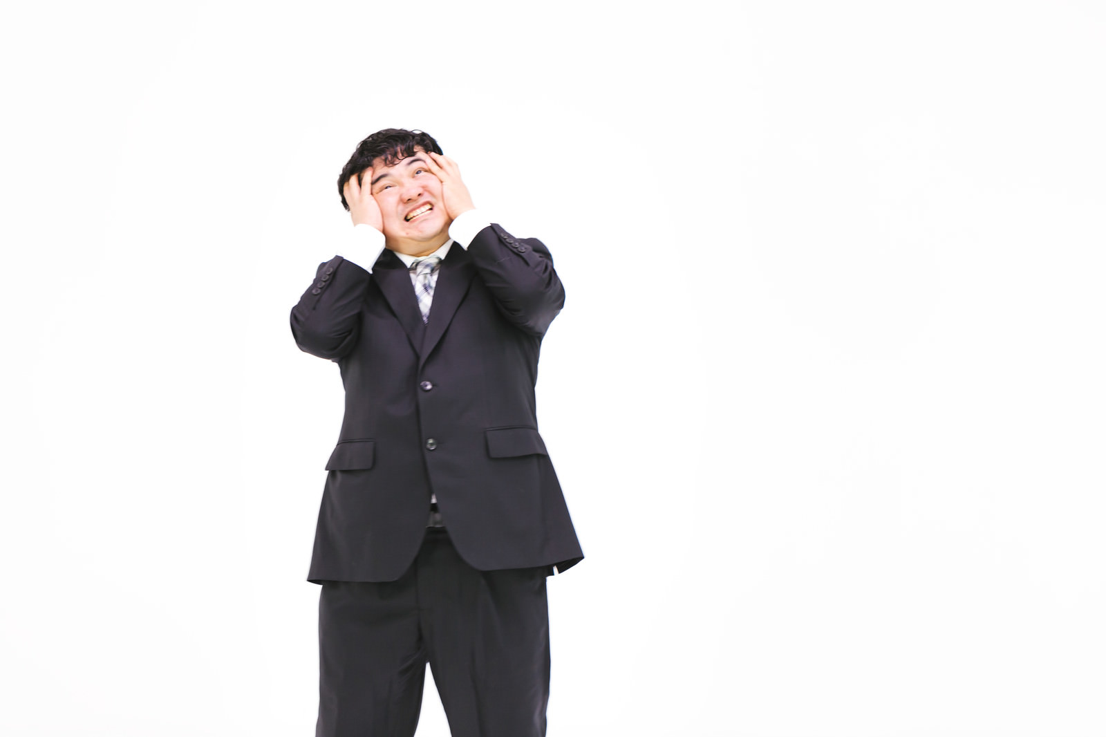 両手で頭を抱えて後悔の表情を浮かべる黒いスーツ姿のサラリーマン［モデル：段田隼人］