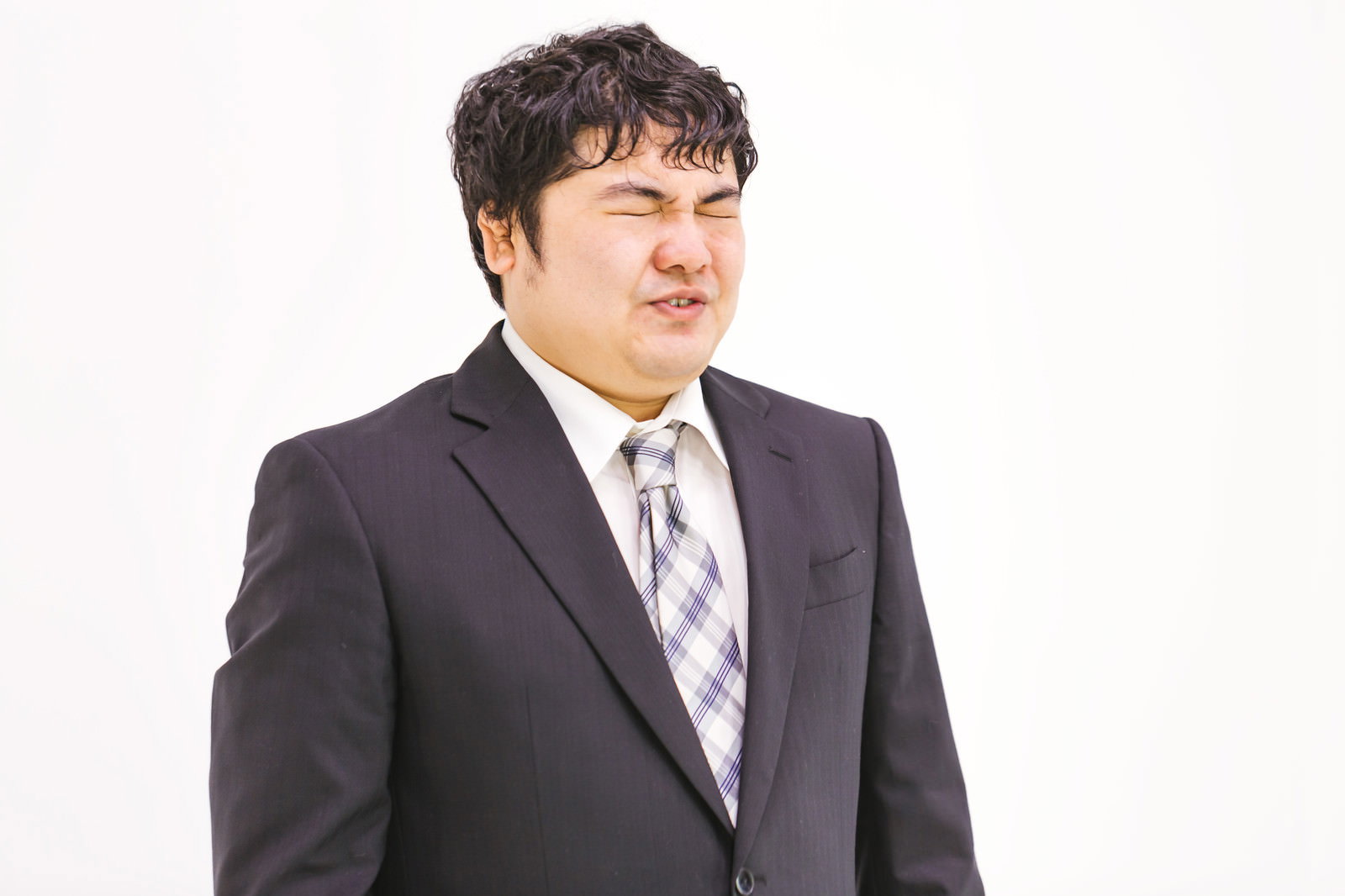 濃紺のスーツを着て困った表情で目を細める会社員男性［モデル：段田隼人］